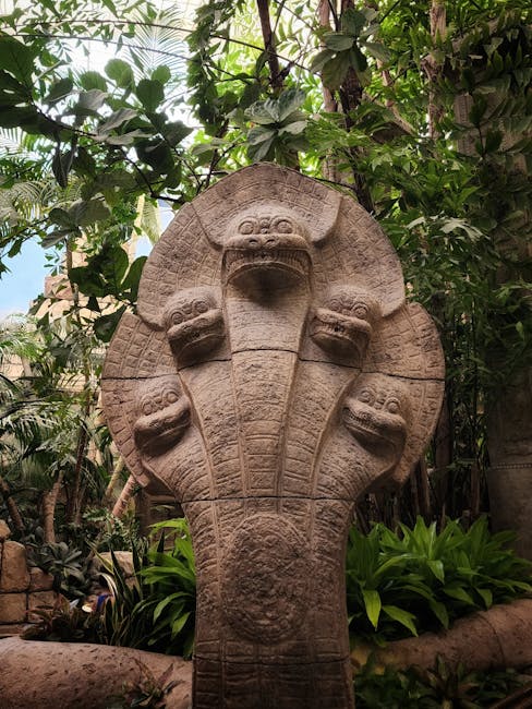 A meerkat perched upright on a large, weathered tree stump in an outdoor setting. The stump has a textured, cracked surface with visible growth rings and jagged edges. Surrounding the stump, there is 
